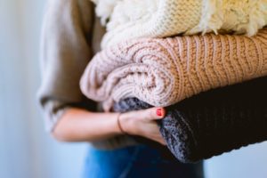 Image: A woman holding a stack of knitted sweaters