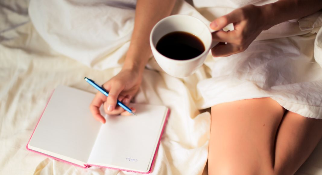 Image: A woman writing in a gratitude journal with a cup of coffee