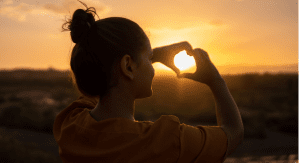 A woman at sunset making a heart shape with her hands (More Self-Love in 2021: 7 Ways to Love Ourselves Daily Rachelle Haime Contributor Miami Mom Collective)