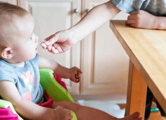 An older sibling feeds a toddler a cracker