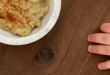 A toddler's hand reaching for a bowl of hummus