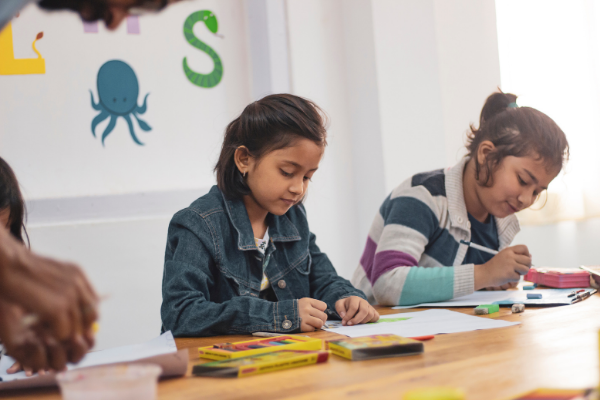 Image: Two girls working side-by-side in a classroom (Moving with Children: 4 Helpful Tips Jessica Socarras Contributor Miami Mom Collective)