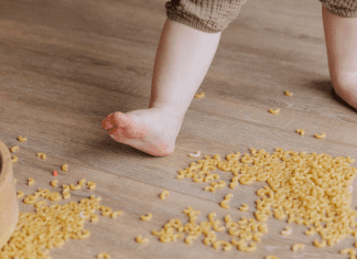 Image of a barefoot toddler stepping in dried macaroni that has spilled on the floor.