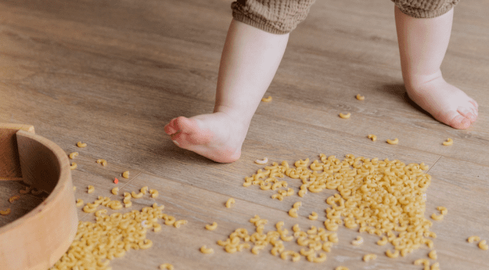 Image of a barefoot toddler stepping in dried macaroni that has spilled on the floor.