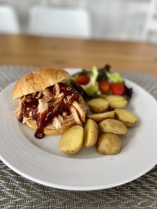 A BBQ pulled chicken sandwich served with roasted potatoes and a salad