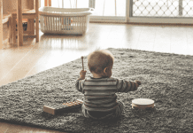 A baby playing on a grey rug in a minimalist room. The baby is playing with musical toys.