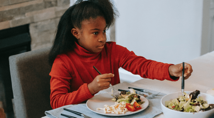 Image: A school-aged girl sitting at a table eating (Raising a Diverse Eater: 3 Keys to Success Dina Garcia Contributor Miami Mom Collective)