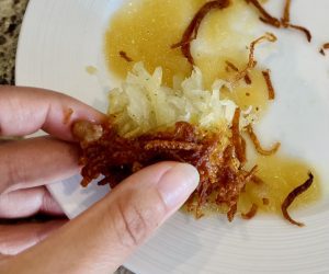 Image: A hand dipping a latke in applesauce (I'm OIL In: Easy Latkes for Hanukkah Rachelle Haime Contributor Miami Mom Collective)