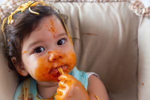 Image: A baby girl with spaghetti sauce all over her face and hands (5 Tips for Your Premature Baby Brittany Aquart Contributor Miami Mom Collective)