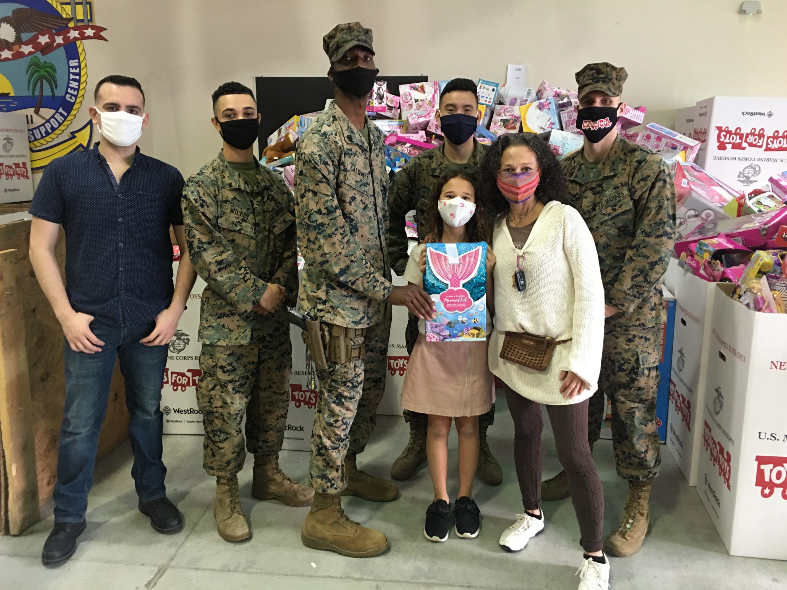 Image: Adita and her daughter with several US Marines standing in front of Toys for Tots collection boxes (Toys for Tots: Making a Difference for America's Children Adita Lang Contributor Miami Mom Collective)