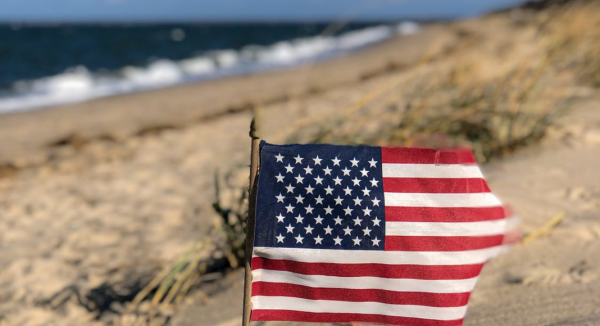 Image: An American flag in the sand with the ocean behind it