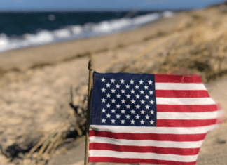 Image: An American flag in the sand with the ocean behind it