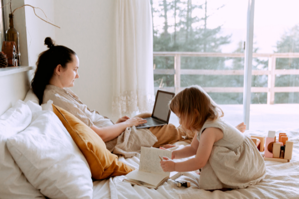 Image: A mom works on her laptop while her daughter plays next to her (5 Tips for the Momtrepreneur Minnie Roca Contributor Miami Mom Collective)