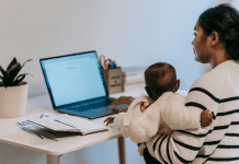 Image: A mom holding her baby while she works at her computer (5 Tips for the Momtrepreneur Minnie Roca Contributor Miami Mom Collective)