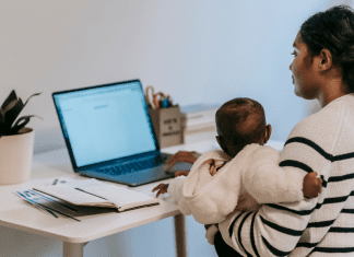 Image: A mom holding her baby while she works at her computer (5 Tips for the Momtrepreneur Minnie Roca Contributor Miami Mom Collective)