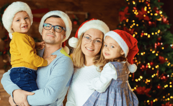 Image; A family wearing Santa hats and standing in front of a Christmas tree (Healthy Holidays: A Survival Guide | Part 2 Dina Garcia Contributor Miami Mom Collective)