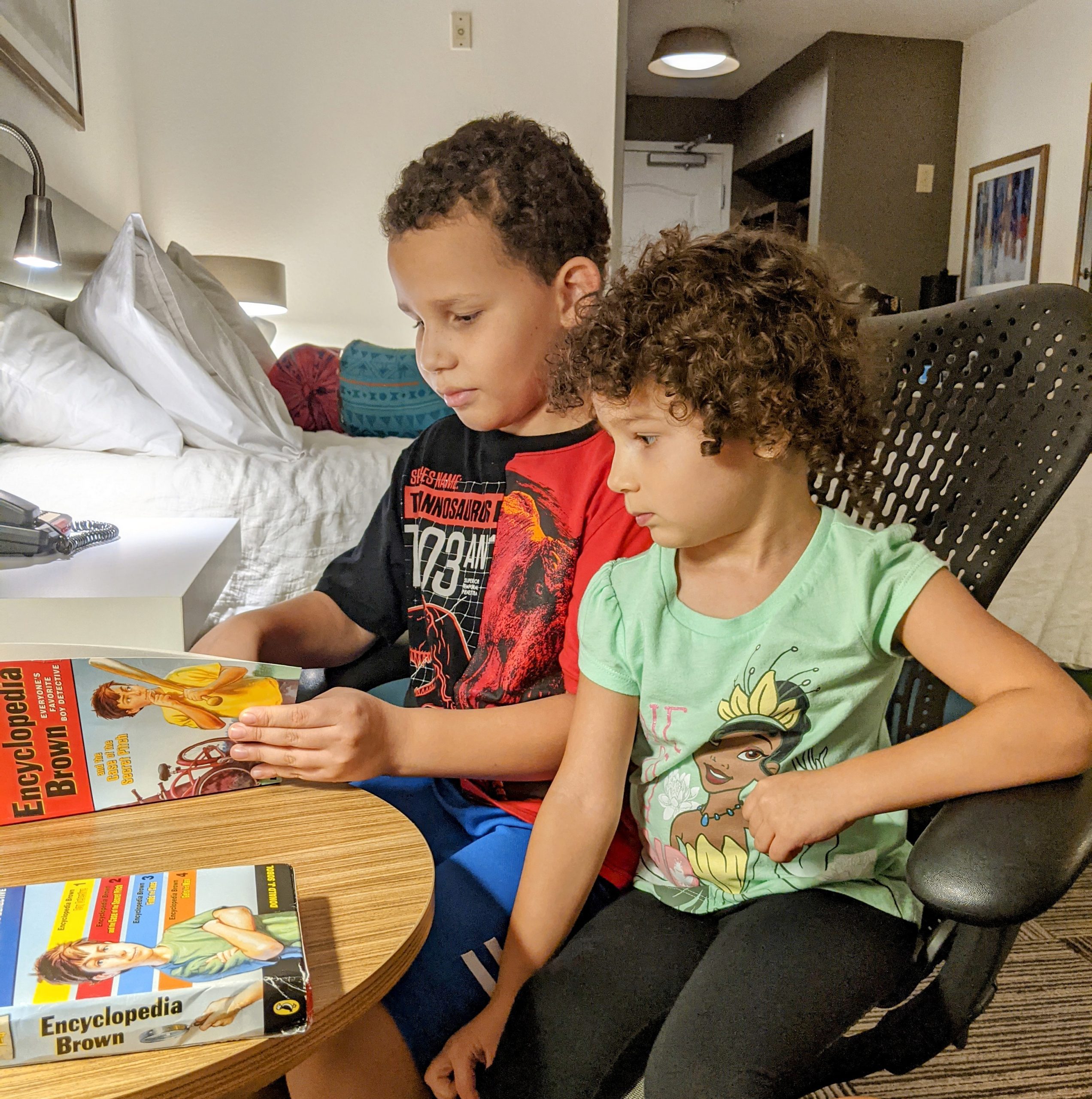 Image: My son reading a book to his sister (Holiday Travel: 3 Ways to Balance Structure & Spontaneity | Dr. Bob Lynda Lantz Editor Miami Mom Collective)