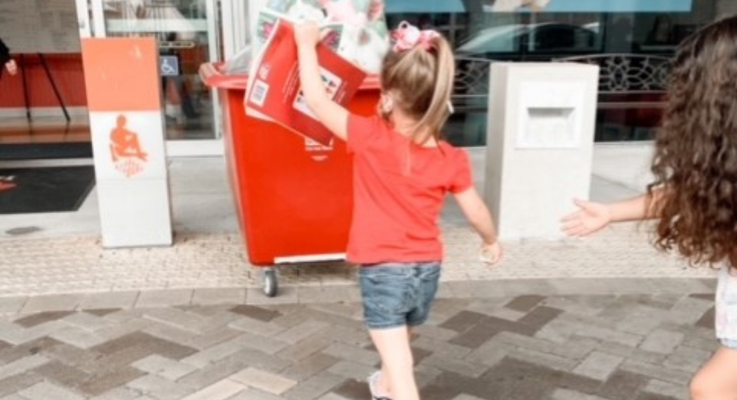 Image: A little girl carrying an item to a toy donation bin (Christmas: An Awesome Opportunity to Volunteer as a Family Holly Farver Contributor Miami Mom Collective)