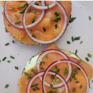 A sliced bagel topped with cream cheese, nova, and sliced red onion