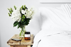 A vase of fresh flowers on a nightstand next to a bed