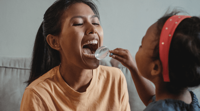 A young girl plays dentist with her mom, holding a magnifying glass up to check her teeth