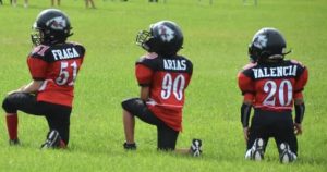 3 pee wee league football players taking a knee on the field