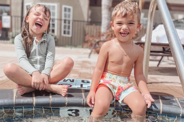 Two kids sitting together by the edge of a pool