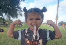 Little girl biting a soccer medal and showing her muscles