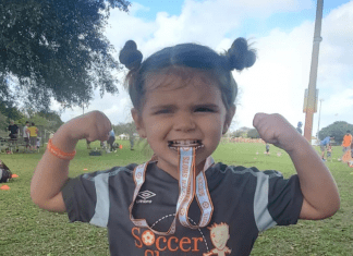 Little girl biting a soccer medal and showing her muscles