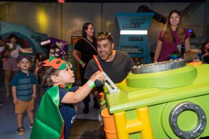A father looks on while his son enjoys the interactive TMNT Secrets of the Sewer Exhibit at Miami Children's Museum