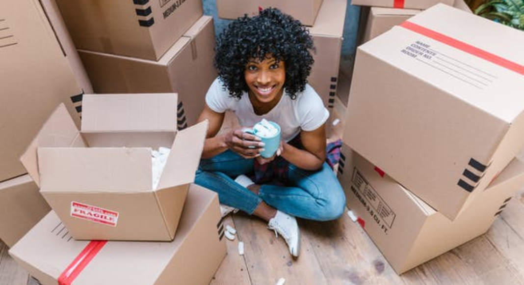 A young woman sits surrounded by moving boxes