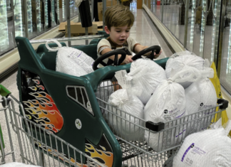 A little boy sits in shopping cart full of frozen turkeys
