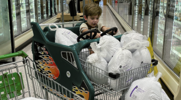 A little boy sits in shopping cart full of frozen turkeys