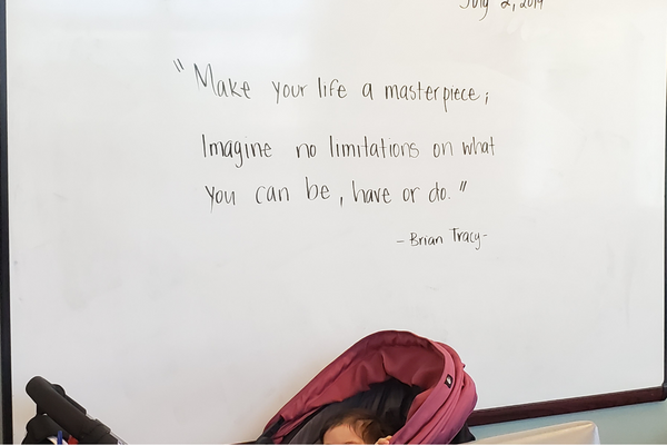Image: An infant in a stroller in front of a white board that reads, "Make you ife a masterpiece. Imagine no limitations on what you can be, have or do." --Brian Tracy