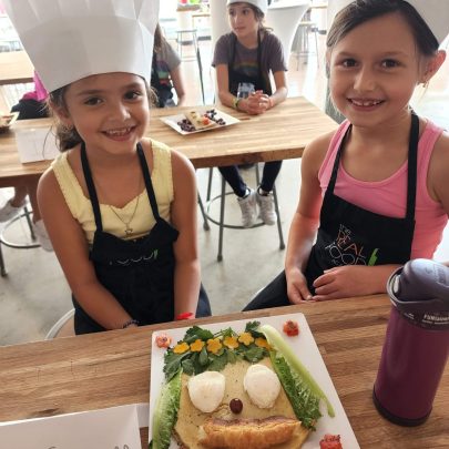 Image: Two children in chefs hats displaying their culinary creation