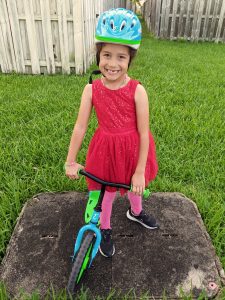 Image: A little girl standing next to a balance bike