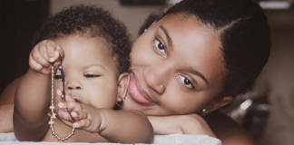 Image: A Black mother smiles while her infant plays