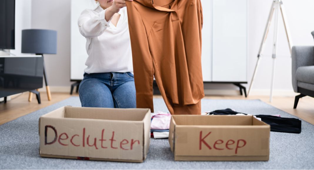 Image: A woman sorts clothing into boxes labeled declutter and keep as a way to give back