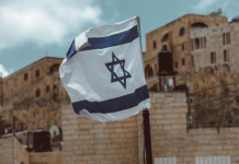 Image: An Israeli flag flies, representing the current world tragedies of war