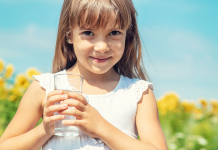 Image: A little girl holds a glass of tap water with a sunflower field in the background