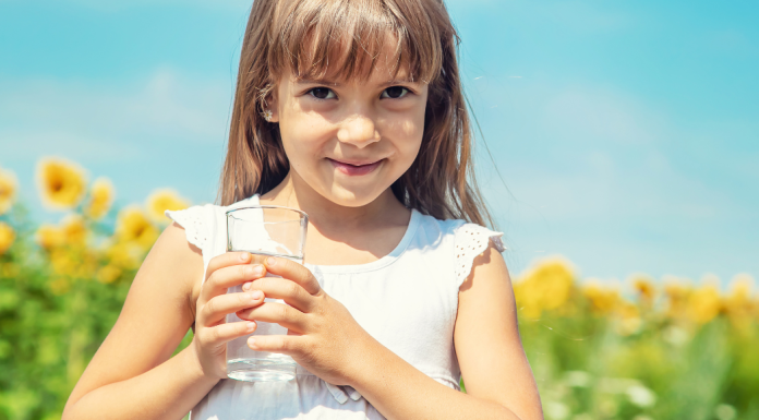 Image: A little girl holds a glass of tap water with a sunflower field in the background