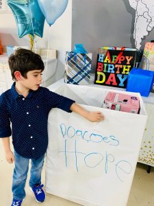 Image: A young boy stands next to a donation collection box at a birthday party