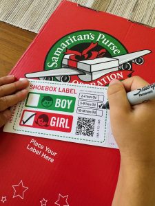 Image: A child fills out a label for a shoebox gift