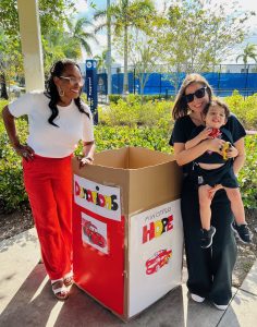 Image: A mother holds her son for a photo with a birthday party guest next to a donation box