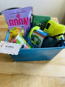 Image: An Easter basket filled with snacks, a Bluetooth beanie, cooling towel, and other items a teen boy might enjoy
