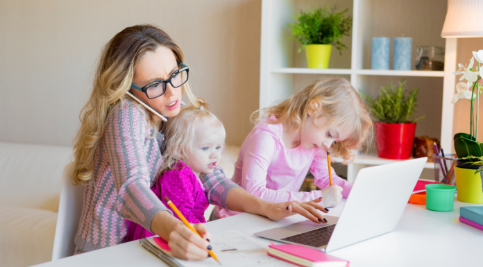 Image: A working mom trying to work from home with a toddler on her lap and a preschooler next to her