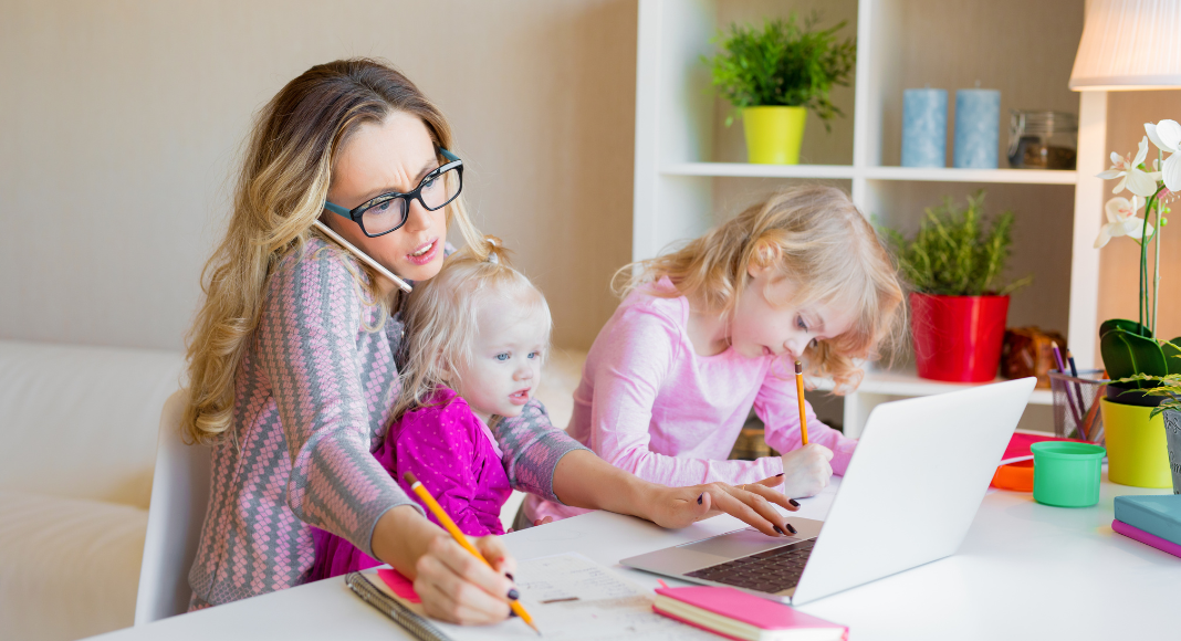 Image: A working mom trying to work from home with a toddler on her lap and a preschooler next to her