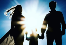 Image: A silhouette of a family holding hands against a blue sky